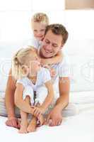Attentive attractive father playing with his children on a bed