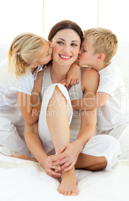 Jolly siblings kissing their mother sitting on a bed