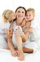 Lively siblings hugging their mother sitting on a bed