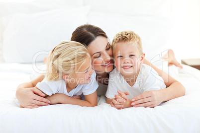 Cute children and their mom having fun lying on a bed
