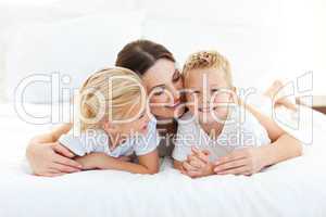 Cute children and their mom having fun lying on a bed