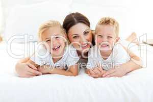 Laughing children playing with their mother lying on a bed