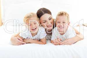 Happy siblings playing with their mother lying on a bed