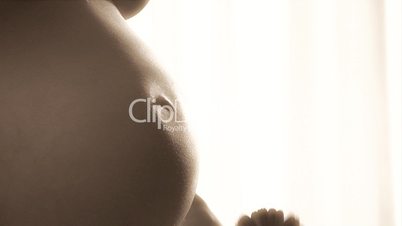 Nude pregnant woman holds flower by her belly