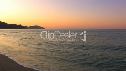 HD Gentle waves on a sandy beach in sunrise, rocks background