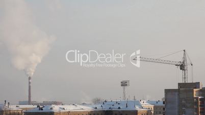 Pipe with smoke and crane in winter sunrise