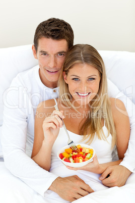 Loving couple eating fruit lying on their bed