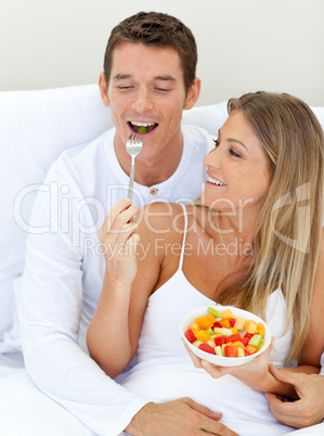 Jolly couple eating fruit lying on their bed