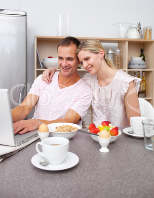Enamored couple using a laptop while having breakfast