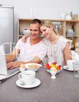 Enamored couple using a laptop while having breakfast