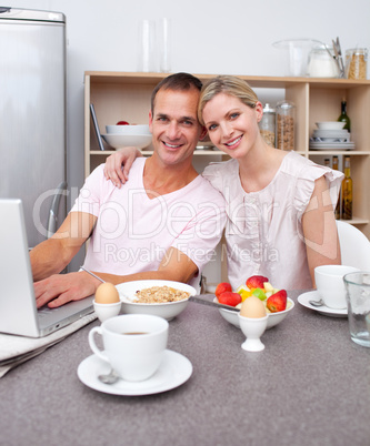 Affectionate couple using a laptop while having breakfast