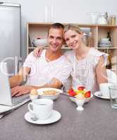 Affectionate couple using a laptop while having breakfast