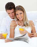Loving couple reading a newspaper and drinking orange juice
