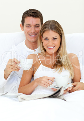 Happy couple drinking coffee lying on their bed