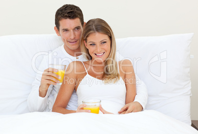 Affectionate couple drinking orange juice lying on their bed