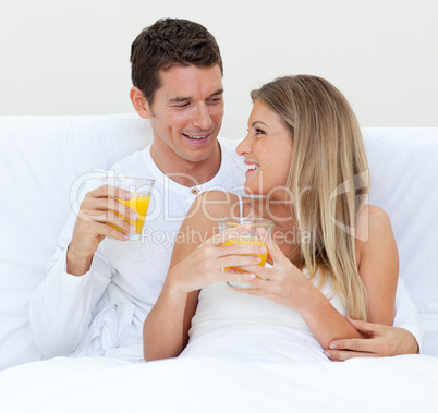 Intimate couple drinking orange juice lying on their bed