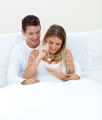 Affectionate couple eating fruit lying on their bed