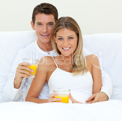 Happy couple drinking orange juice lying on their bed