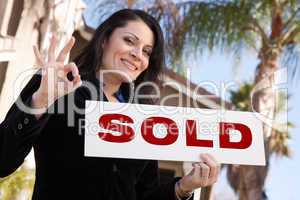 Attractive Hispanic Woman Holding Sold Sign In Front of House