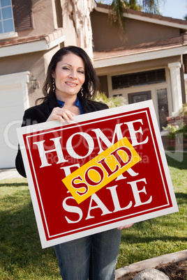 Hispanic Woman Holding Red Sold Real Estate Sign In Front of Hou