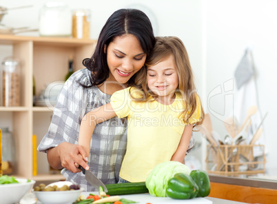 child cutting vegetables with her mother