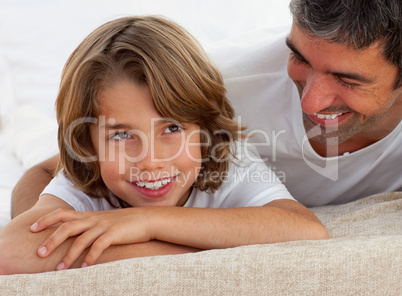 Cute little boy having fun with his father lying on bed