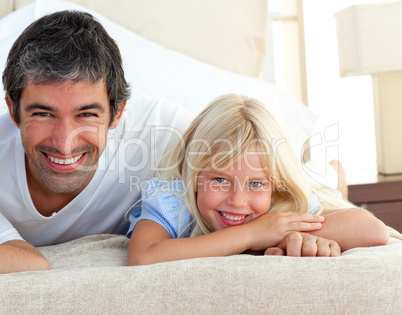 Smiling little girl having fun with her father lying on bed