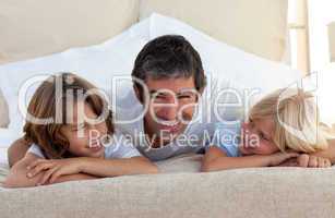Smiling father talking with his children lying on bed