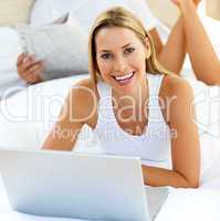 Smiling woman using a laptop lying on bed
