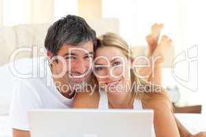 Enamoured couple using a laptop lying on bed