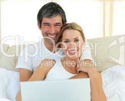 Smiling couple using a laptop lying in the bed