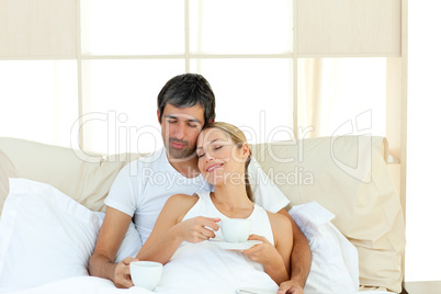 Positive couple drinking coffee lying in the bed