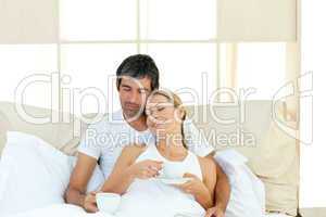 Positive couple drinking coffee lying in the bed