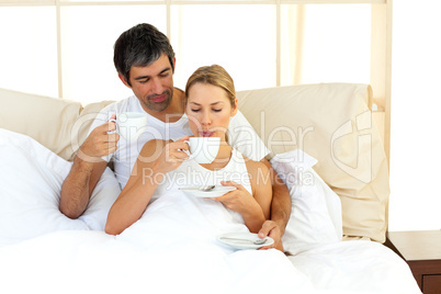 Jolly couple drinking coffee lying in the bed
