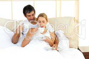 Jolly couple drinking coffee lying in the bed