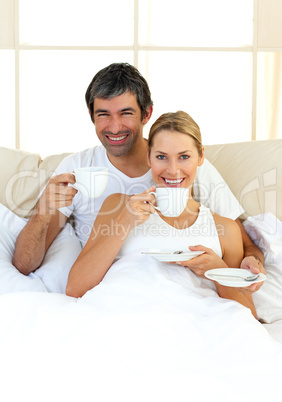 Enthusiastic lovers drinking coffee lying in the bed