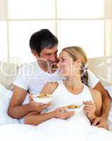 Cheerful lovers eating cereals lying in the bed