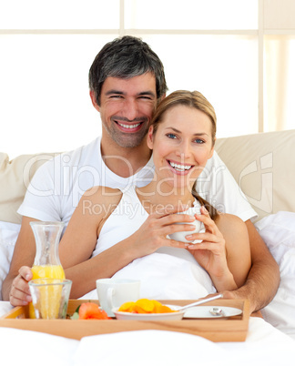 Smiling couple having breakfast lying in the bed