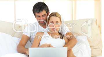 Affectionate couple using a laptop lying in the bed
