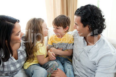 Cute siblings sitting on sofa with their parents
