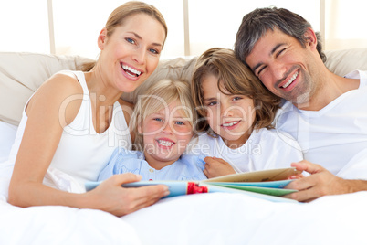 Smiling family reading a book on bed