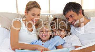 Joyful family reading a book on bed