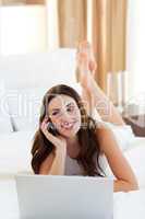 Jolly woman on phone using her laptop lying on bed