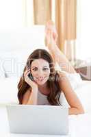 Beautiful woman on phone using her laptop lying on bed