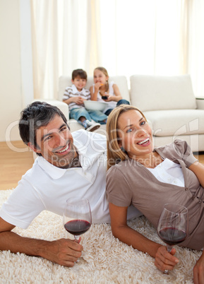 Smiling lovers drinking wine lying on the floor