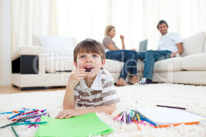 Pensive little boy drawing lying on the floor