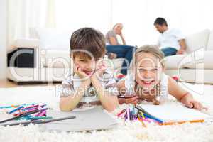 Smiling siblings drawing lying on the floor