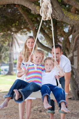 Joyful parents pushing their children on a swing