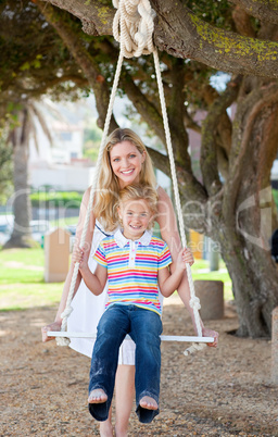 Caring mother pushing her daughter on a swing