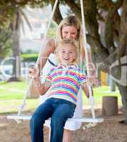Jolly mother pushing her daughter on a swing